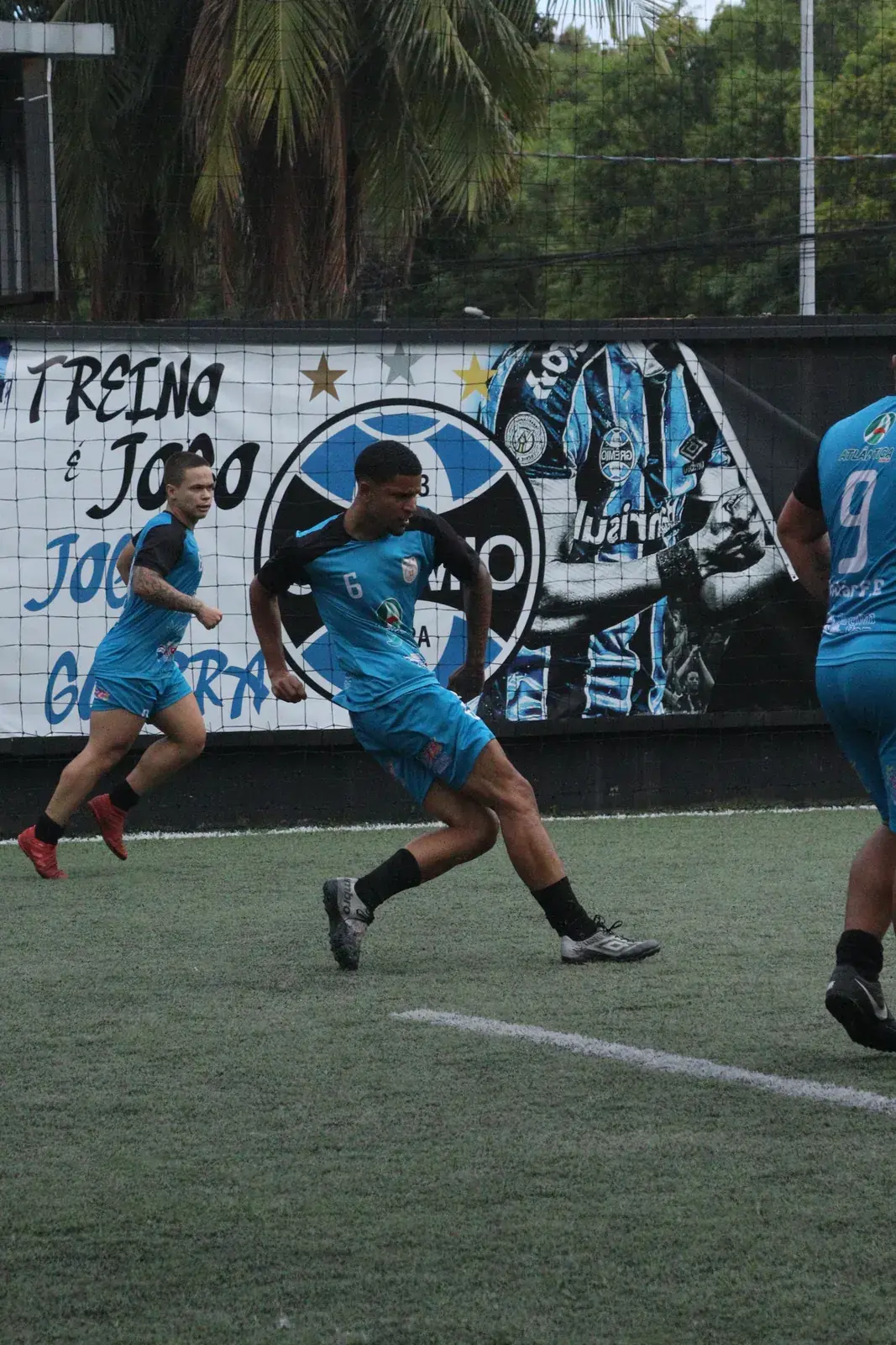 Jogador conduz a bola diante do painel do Grêmio no campo do Quintal