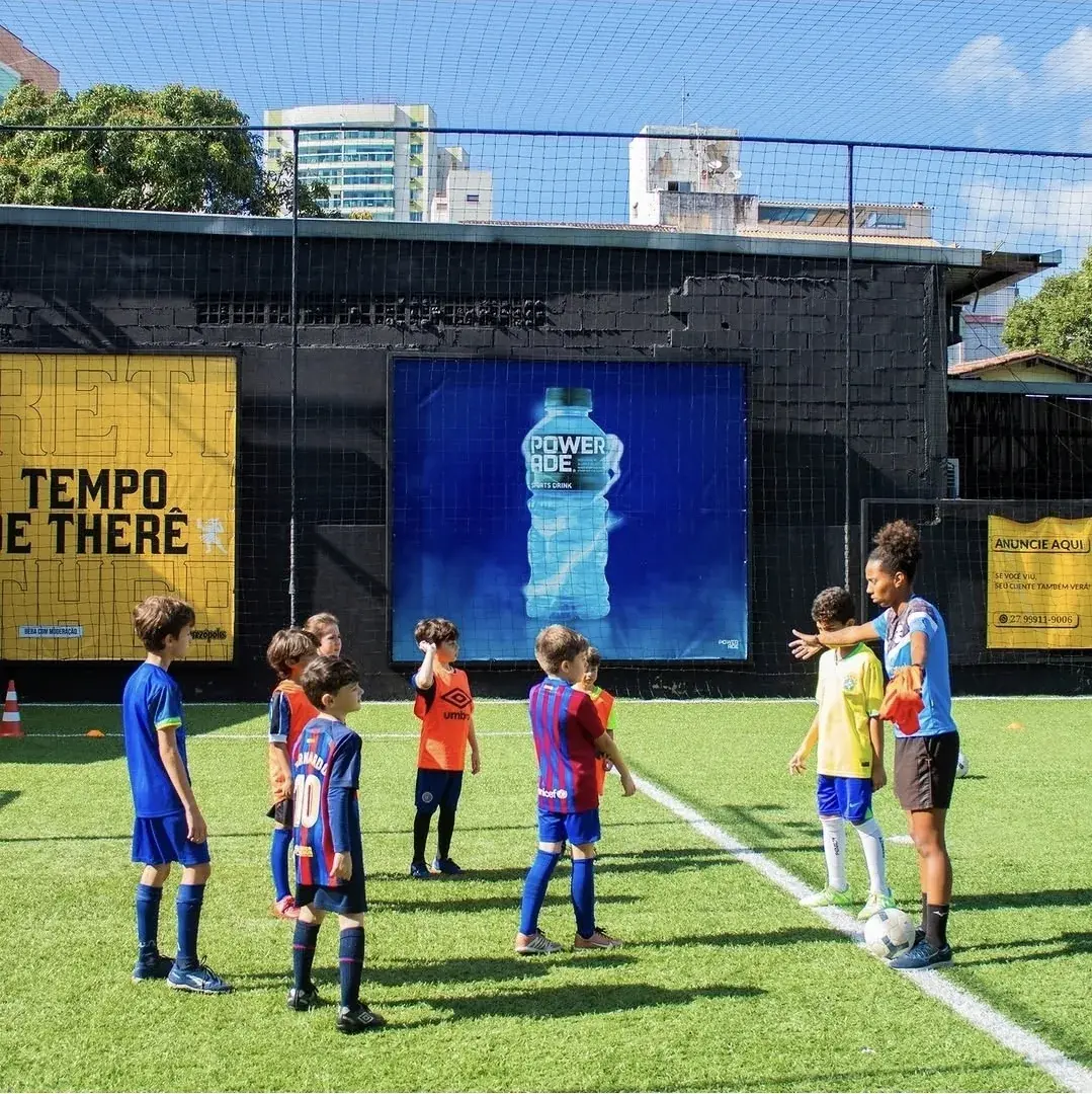 Professora orientando crianças da escolinha de futebol no campo do Quintal